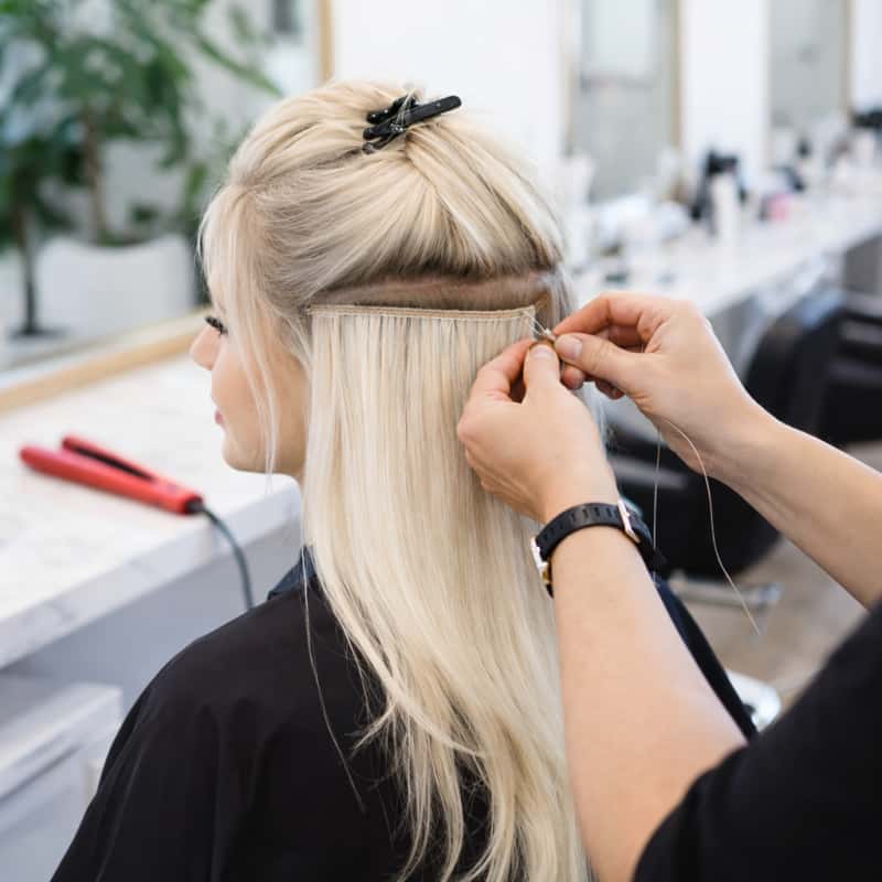 Genius Weft Platinum Application Person getting a hair extension fitted by a hairstylist in a salon setting.